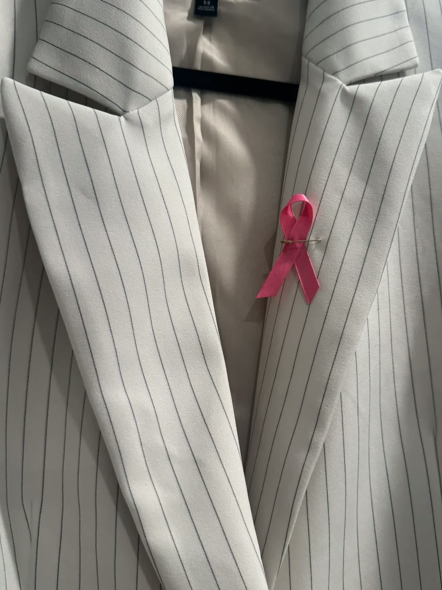 Pink breast cancer awareness ribbon pinned to a pinstripe blazer